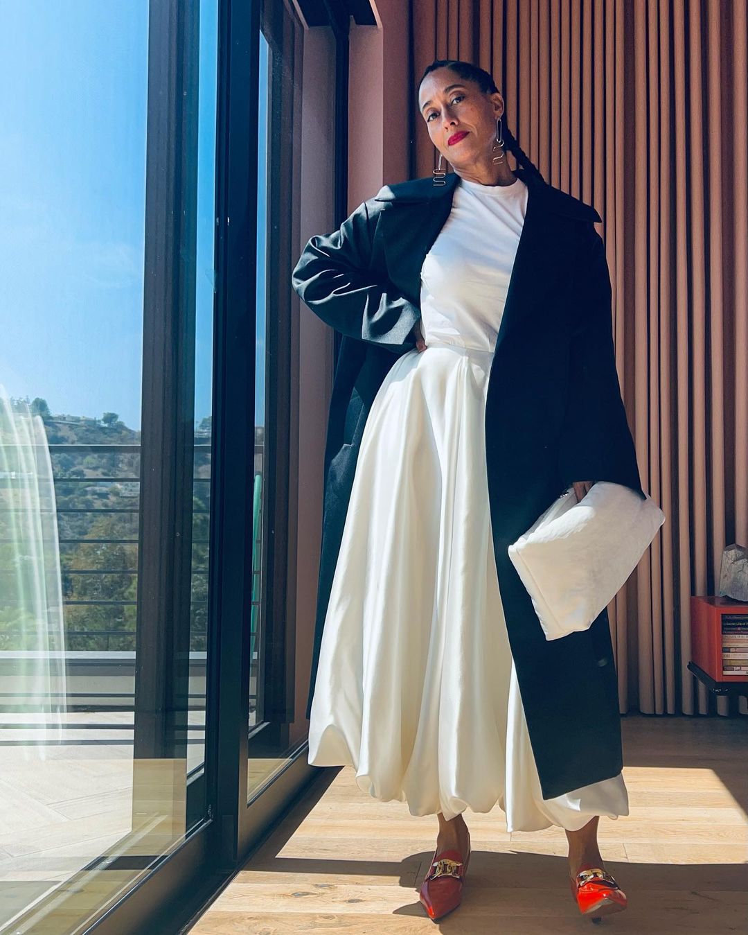 Tracee Ellis Ross wears a white dress, trench coat and red heels.