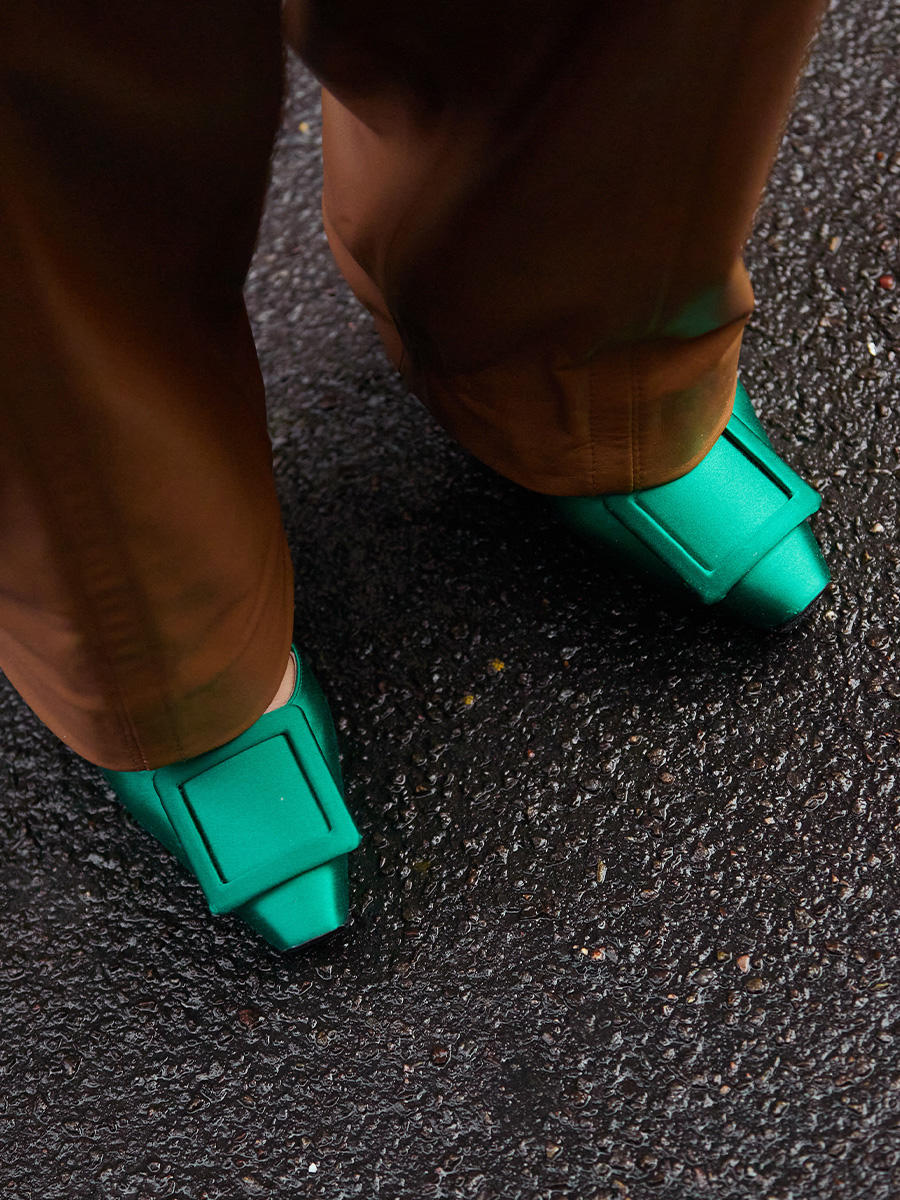 Приталенные коричневые брюки сочетаются с ярко-зелеными туфлями на каблуке.