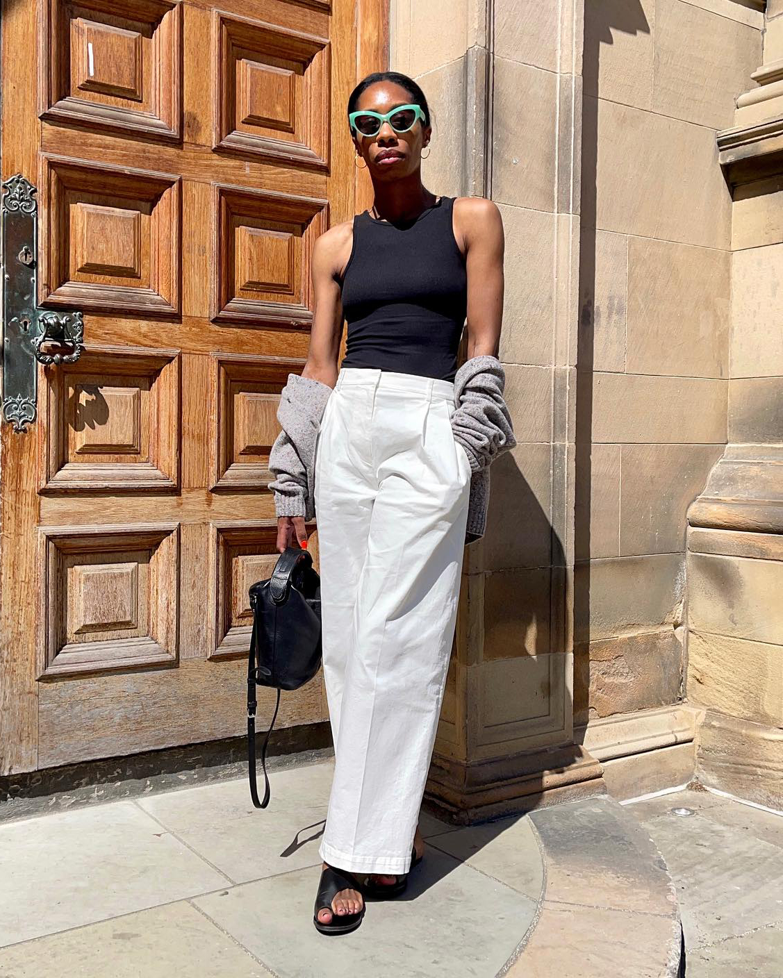 Outfit ideas 2023: Louisa Hatt wears a black tank top with white trousers and sandals.